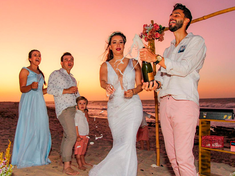 Noivo estourando champanhe comemorando casamento junto com a noiva e convidados na praia